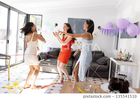 Dancing joyfully in sunlit living room, three young women celebrate together Dancing joyfully in sunlit living room, three young women celebrate together 135541510