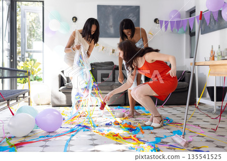 Cleaning up colorful streamers and balloons, three women enjoy festive gathering at home Cleaning up colorful streamers and balloons, three women enjoy festive gathering at home 135541525