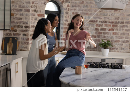 Laughing and chatting, three young women gather in stylish kitchen 135541527