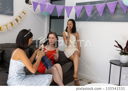 Opening gift bag, three young women celebrate at birthday party at home 135541531