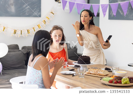Celebrating birthday, three women gather around table with chocolate cake Celebrating birthday, three women gather around table with chocolate cake 135541533