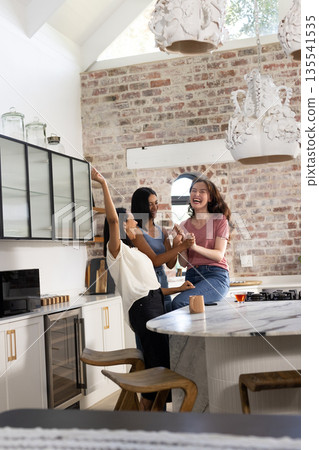 Laughing and dancing in modern kitchen, three young women enjoy each other's company 135541535