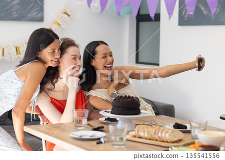 Laughing and taking selfie, three young women celebrate at birthday party Laughing and taking selfie, three young women celebrate at birthday party 135541556