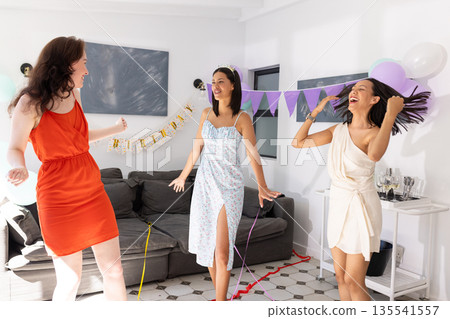 Dancing joyfully in living room, three young women celebrate together Dancing joyfully in living room, three young women celebrate together 135541557