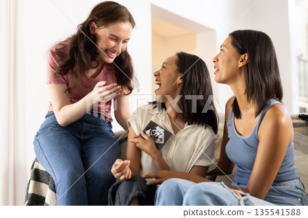 Laughing together on cozy couch, three young women share joyful moments 135541588