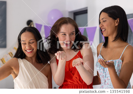Laughing and celebrating, three young women enjoy festive gathering at home 135541598