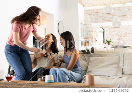 Laughing and chatting, three women enjoy cozy afternoon at home Laughing and chatting, three women enjoy cozy afternoon at home 135541602