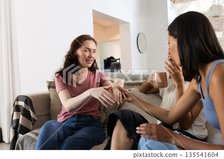 Laughing and chatting, three young women relax on cozy sofa at home 135541604