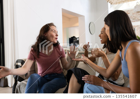 Engaging in animated conversation, three young women sit together on cozy sofa 135541607