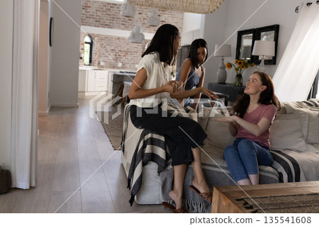 Chatting and laughing, three young women relax in cozy living room 135541608