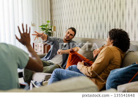Friends relaxing on sofa, enjoying conversation and laughter in cozy living room Friends relaxing on sofa, enjoying conversation and laughter in cozy living room 135541648
