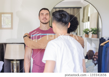 Groom getting measured for suit fitting, surrounded by friends, smiling warmly Groom getting measured for suit fitting, surrounded by friends, smiling warmly 135541656