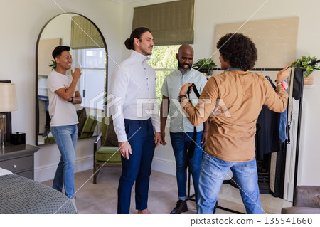 Groom preparing with friends, adjusting tie and sharing laughter in bedroom Groom preparing with friends, adjusting tie and sharing laughter in bedroom 135541660