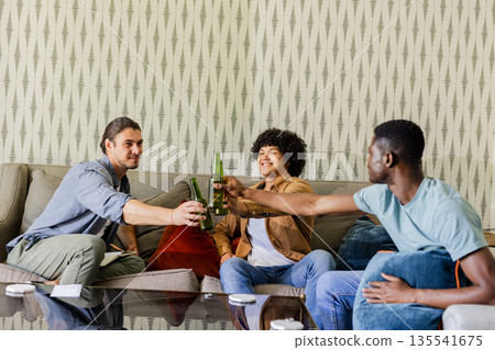 Friends celebrating with drinks on sofa, enjoying joyful moments together indoors 135541675