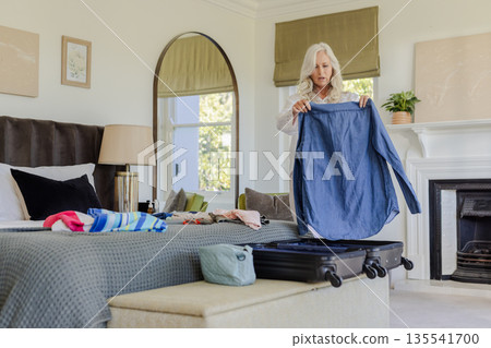Woman packing suitcase in bedroom, organizing clothes for upcoming trip Woman packing suitcase in bedroom, organizing clothes for upcoming trip 135541700