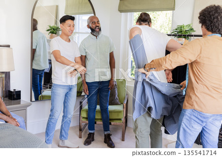 Groomsmen helping groom try on suit jacket, preparing for wedding ceremony Groomsmen helping groom try on suit jacket, preparing for wedding ceremony 135541714
