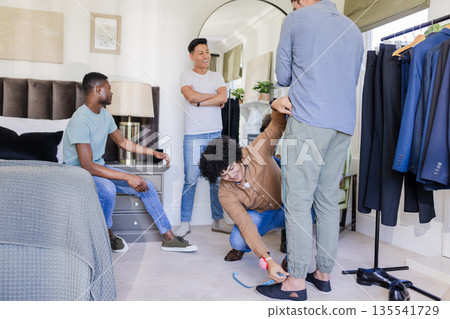 Groom and friends preparing suits, measuring pants in bedroom before wedding 135541729
