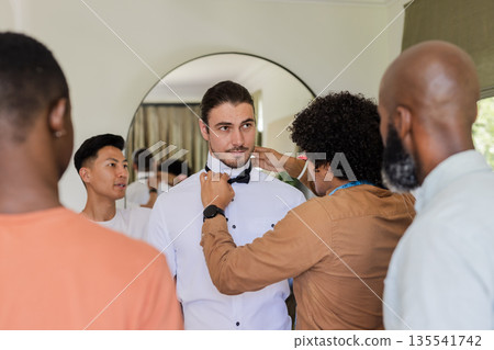 Groom getting ready with friends adjusting bow tie in elegant room Groom getting ready with friends adjusting bow tie in elegant room 135541742