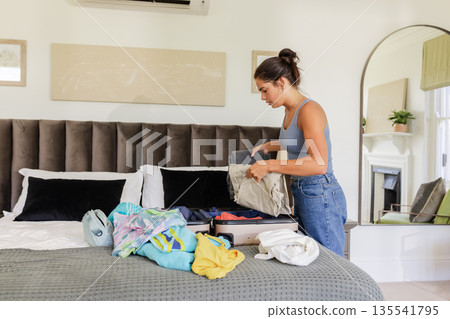 Woman packing suitcase on bed, preparing for wedding trip with focus and care 135541795