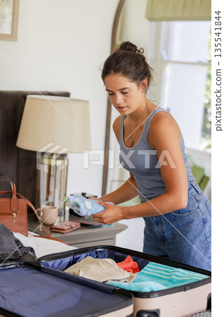 Woman packing suitcase in bedroom, preparing for travel with focused expression Woman packing suitcase in bedroom, preparing for travel with focused expression 135541844