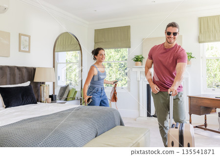 Couple arriving in hotel room, smiling and carrying luggage, ready for vacation Couple arriving in hotel room, smiling and carrying luggage, ready for vacation 135541871