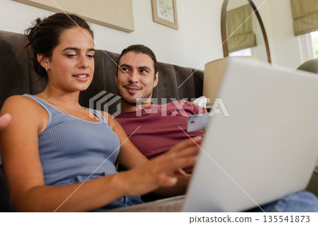 Couple shopping online using laptop, smiling and enjoying time together at home 135541873