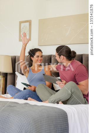 Couple sitting on bed, smiling and using digital tablets at home Couple sitting on bed, smiling and using digital tablets at home 135541876