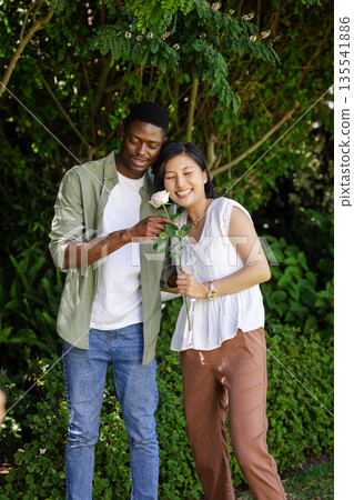 Couple enjoying romantic moment in garden, holding rose and smiling together Couple enjoying romantic moment in garden, holding rose and smiling together 135541886