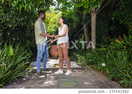 African American man and Asian woman holding hands in garden, sharing moment African American man and Asian woman holding hands in garden, sharing moment 135541892