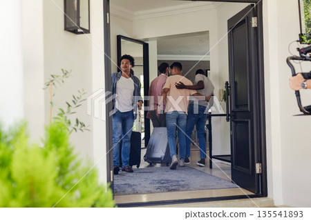 Friends arriving at home, carrying luggage and hugging, preparing for celebration Friends arriving at home, carrying luggage and hugging, preparing for celebration 135541893