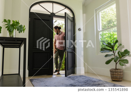 Man entering home through open door, looking outside with curiosity 135541898