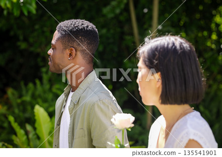 Holding white rose, African American man and Asian woman at garden wedding ceremony 135541901