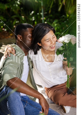 Embracing and smiling, African American man and Asian woman with flowers outdoors 135541912