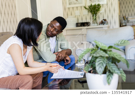 Couple discussing wedding plans at home, reviewing documents with focus and care 135541917