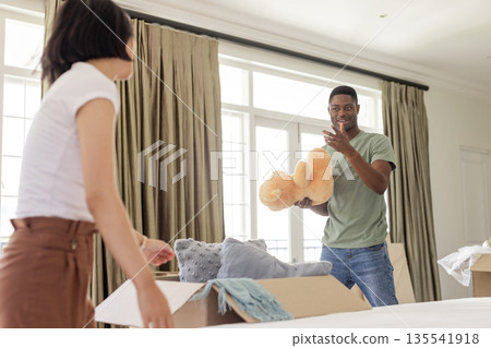 Couple unpacking boxes at home, smiling and holding teddy bear together Couple unpacking boxes at home, smiling and holding teddy bear together 135541918