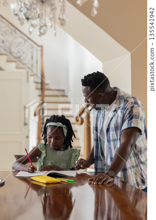 African American father helping daughter with homework at home, both concentrating 135541942