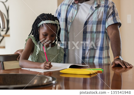 Father helping daughter with homework at kitchen table, both smiling and engaged 135541948