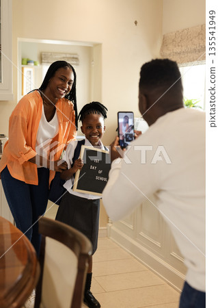 African American father taking picture of daughter holding first day of school sign 135541949