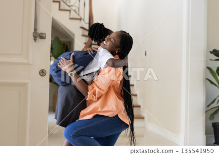 African American mother hugging daughter at home, both smiling warmly African American mother hugging daughter at home, both smiling warmly 135541950