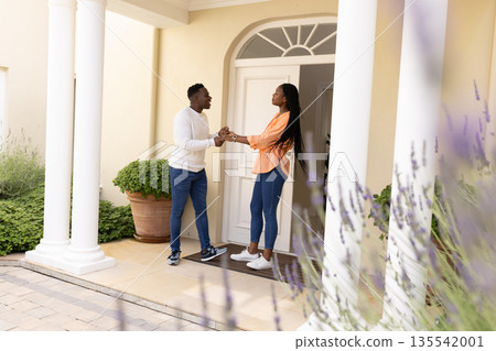 Couple holding hands and smiling warmly on front porch of their home 135542001