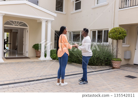 African American couple standing outside home, holding hands and smiling warmly 135542011