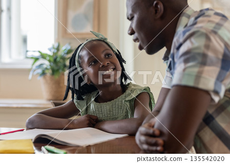 Father and daughter smiling while doing homework together at home Father and daughter smiling while doing homework together at home 135542020