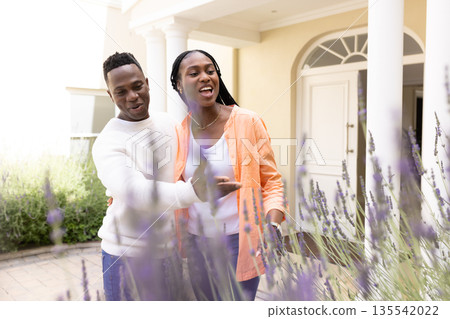 Couple enjoying garden walk, smiling and pointing at blooming lavender plants 135542022