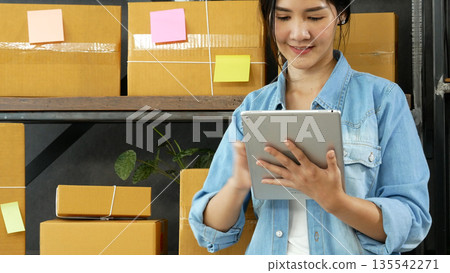 Asian woman startup small business at home office. Online seller entrepreneur young asian woman use tablet checking online order. Woman using tablet check stock goods supply delivery package shipping 135542271
