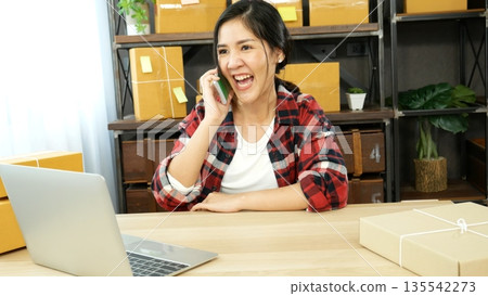 Online seller entrepreneur young asian woman using phone calling, checking online order. Woman calling check goods stock, delivery package shipping. Asian woman startup small business at home office 135542273