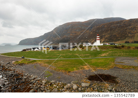 Lighthouse standing on a green meadow with coastal sea and mountains in the background in Norway. 135542789