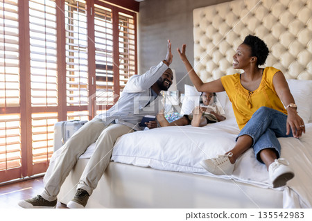 Family enjoying quality time, parents giving high five on bed with child Family enjoying quality time, parents giving high five on bed with child 135542983
