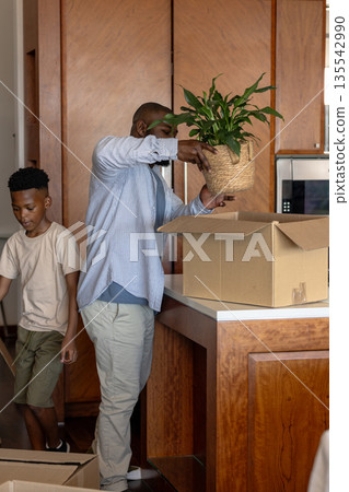 Father and son unpacking boxes in kitchen, placing plant on counter Father and son unpacking boxes in kitchen, placing plant on counter 135542990