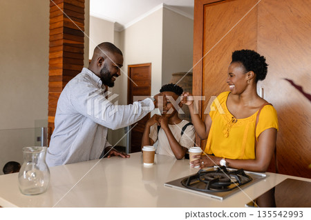 Family enjoying morning coffee together in kitchen, sharing happy fist bumps 135542993
