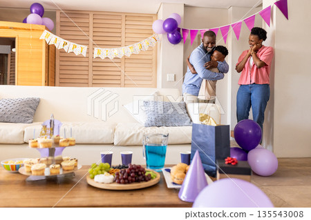 Family celebrating birthday at home, hugging and smiling with festive decorations 135543008